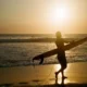 Surfer walking along Batu Bolong Beach at sunset in Canggu, Bali