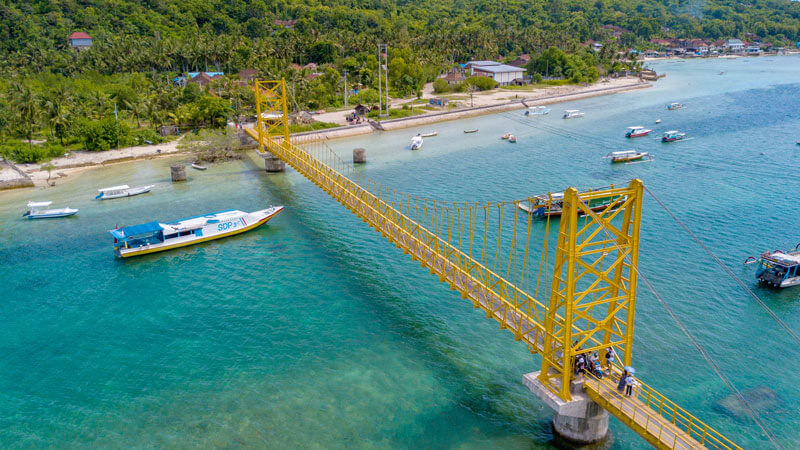 The iconic Yellow Bridge in Nusa Lembongan, Bali, with blue sea and boats in the background