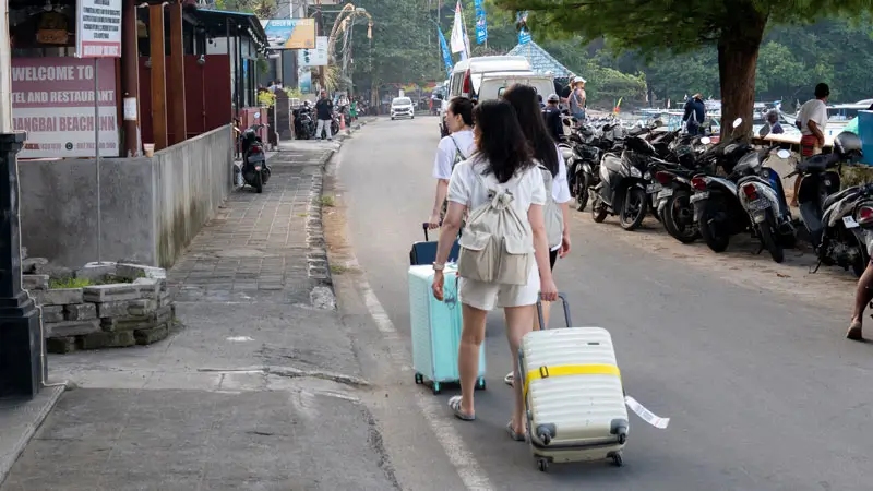 Tourists walking with luggage towards the speedboat departure point in Bali