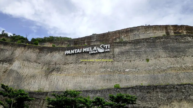 The name of Melasti Ungasan Beach is displayed on a high limestone cliff