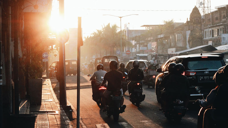 Busy street in Bali at sunset with motorbikes and cars, highlighting local transportation options.