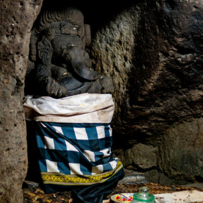 Statue of Lord Ganesha draped in a traditional checkered cloth in the Goa Gajah Temple cave