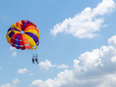 Tourists parasailing against a backdrop of bright blue sky and fluffy clouds in Bali.