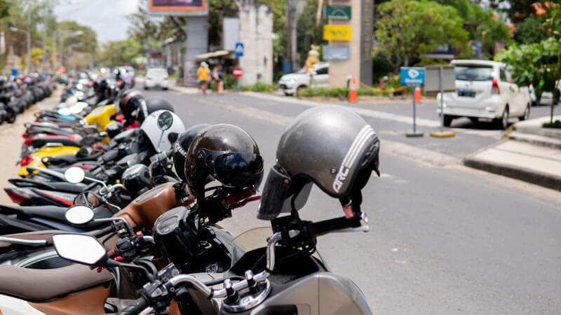 Row of parked motorbikes with helmets in Bali, a popular mode of transport for tourists.