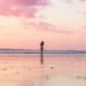 Silhouette of a woman walking on Bali beach at sunset with a pink sky.