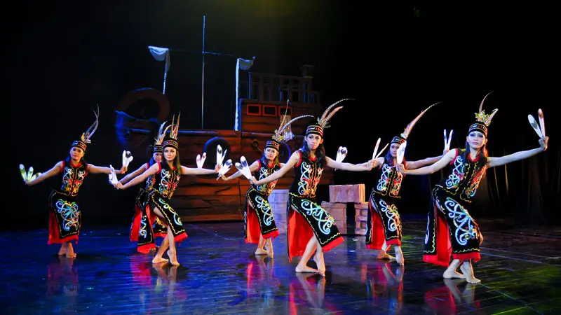 Bali performers in traditional Borneo costumes performing a cultural dance on stage with vibrant choreography. Image Credit: © Devdan