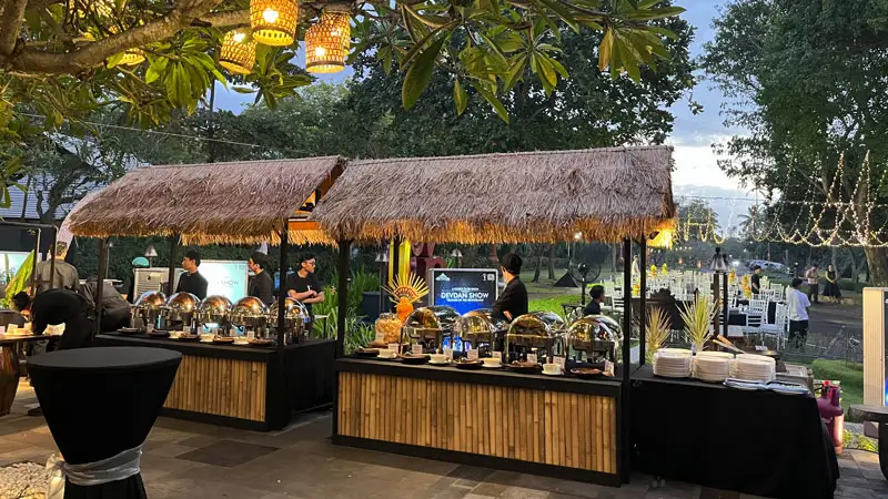 Outdoor buffet setup with traditional thatched roofs offering dinner for guests. © DevdanBali