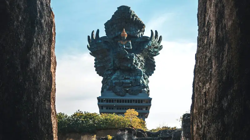 The towering Garuda Wisnu Kencana statue in Bali, framed between two limestone cliffs, showcasing its intricate design and cultural significance.