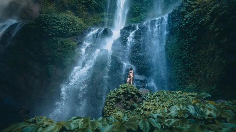 A traveler standing on a rock in front of Sekumpul Waterfall, one of the best places to visit in Bali.