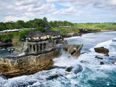 Tanah Lot Temple perched on a rocky outcrop in the ocean, surrounded by waves and lush greenery in Bali.