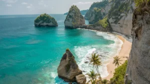 View of Nusa Penida Beach in Bali with clear blue sea water, white sand, coconut trees and beautiful coral rock formations.