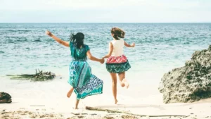 Two travelers holding hands and jumping on a beautiful beach in Bali, showcasing the excitement and adventure of a Bali trip.