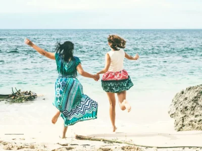 Two travelers holding hands and jumping on a beautiful beach in Bali, showcasing the excitement and adventure of a Bali trip.