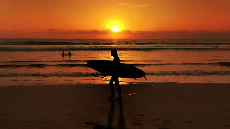 Silhouette of surfer carrying surfboard at sunset at Kuta Beach