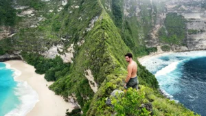 Man standing on cliff at Kelingking Beach, Nusa Penida, with turquoise waves below