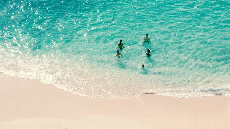 Families swimming in the shallow, clear waters of Pandawa Beach Bali.