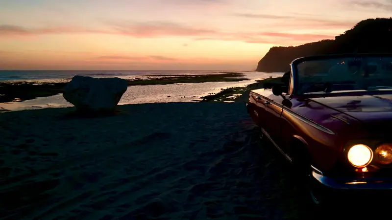 Stunning sunset view at Pandawa Beach Bali with a vintage car in the foreground.