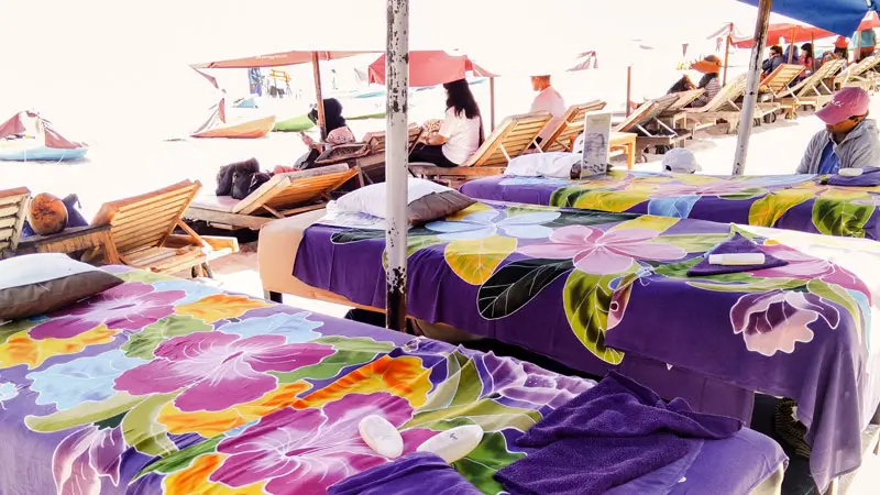 Colorful massage beds set up on the sand for traditional Balinese massage.