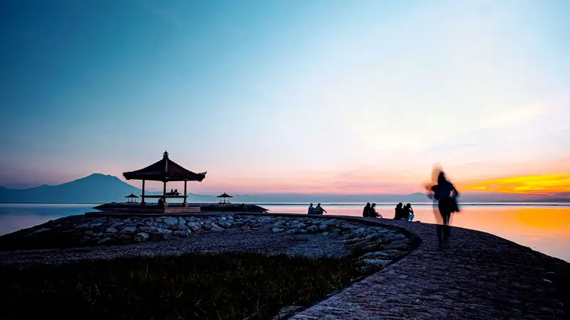 Silhouettes of visitors enjoying a vibrant sunrise with a traditional gazebo in view.