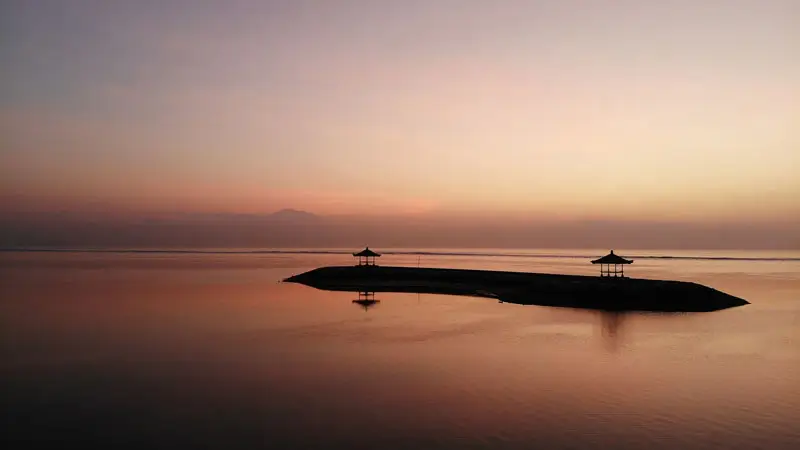 Peaceful sunrise view at Sanur Beach, Bali, featuring a gazebo reflection on calm waters.