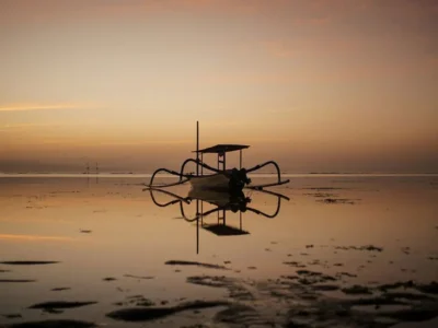 Sunrise at Sanur Beach Bali with a traditional jukung boat reflecting on the calm waters.